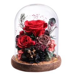 a glass dome with red roses and greenery in the center on a wooden base