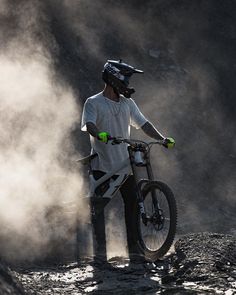 a man standing next to a mountain bike in the dirt with steam coming out of it