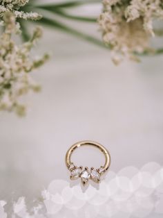 three stone ring sitting on top of a white table next to flowers and greenery