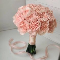 a bouquet of pink carnations tied to a white table with ribbon on it