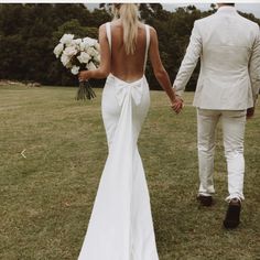 a bride and groom walking hand in hand through the grass holding hands with each other