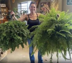 a woman holding two large potted plants in her hands