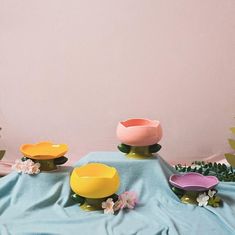 three bowls are sitting on a table with flowers and leaves around them, one is pink