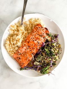 a white plate topped with salmon, rice and veggies next to a fork