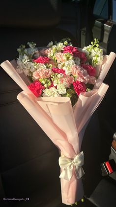 a bouquet of flowers sitting in the back seat of a car, wrapped in pink and white paper