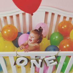 a baby in a crib surrounded by balloons