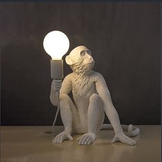 a statue of a monkey holding a light bulb in its hand and sitting on the ground