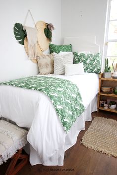 a white bed with green and white pillows on top of it next to a window