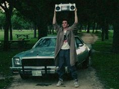 a man holding up an old radio above his head in front of a parked car