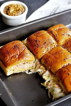 a pan filled with rolls covered in meat and cheese next to a bowl of seasoning