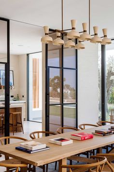 the dining room table is surrounded by wooden chairs and tables with books on them in front of glass doors