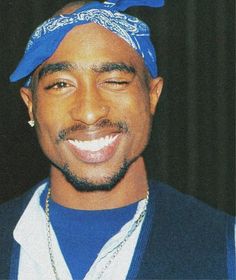 a man with a blue bandana on his head smiling at the camera while wearing a necklace