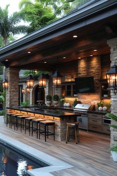 an outdoor kitchen with bar seating and grill on the deck by the pool is surrounded by palm trees