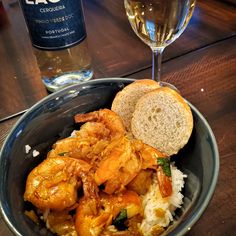 a bowl filled with rice and shrimp next to a glass of wine