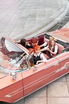 three women sitting in the back of a red convertible car with their hair pulled back