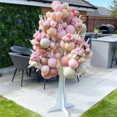 a tree made out of balloons in a backyard with an outdoor dining area behind it