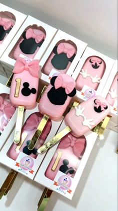 there are many pink cake shaped like minnie mouses in the box with gold forks