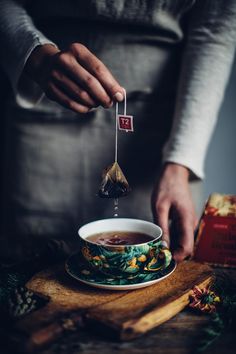 a person is holding a tea bag in their hand and stirring it into a cup