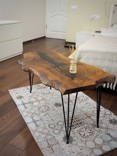 a wooden table with hairpin legs on a rug in a living room next to a bed