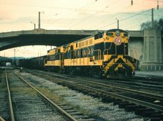 a yellow and black train traveling under a bridge