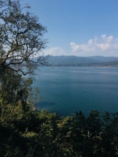 a lake surrounded by trees with mountains in the distance and blue sky above it, on a sunny day