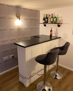 two bar stools sitting in front of a counter with bottles on top of it