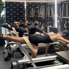 two women are doing exercises on machines in a room with mirrors and black walls behind them