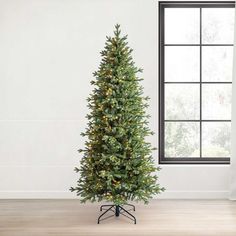 a tall artificial christmas tree with lights on it in front of a white wall and window