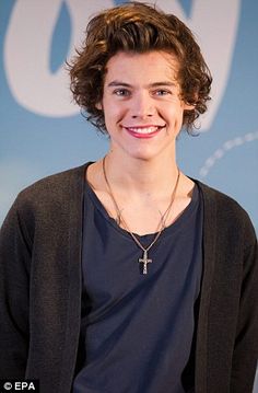 a smiling young man wearing a black cardigan and standing in front of a blue wall