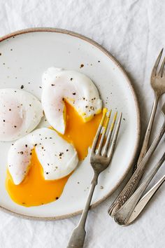 two fried eggs are on a plate with silverware