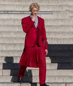 a man in a red suit and tie standing on steps with his hand to his face