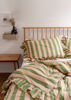 a bed with green and pink striped comforter on it next to a wooden headboard