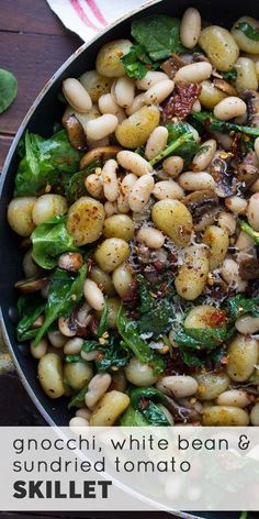 a skillet filled with white bean and spinach salad on top of a wooden table