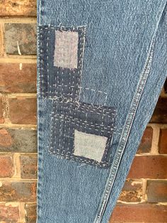 an old pair of jeans with patchwork on them hanging up against a brick wall