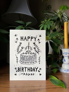 a happy birthday card sitting on top of a table next to a candle and potted plant