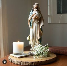 a statue of the virgin mary with flowers and a candle on a table next to a book