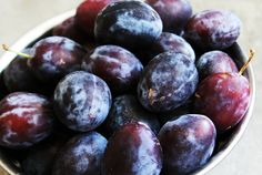 a white bowl filled with plums on top of a table