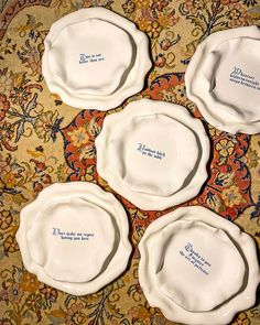 four white plates with blue writing on them sitting on a rug in front of a floral design