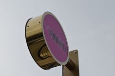 a pink and gold street sign sitting on top of a metal pole under a gray sky