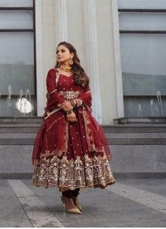 a woman standing in front of a building wearing a red and gold dress with intricate details