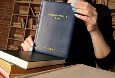 a woman sitting at a table with a book in front of her, reading human rights law