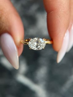 a woman's hand holding a ring with a diamond on it and white nails