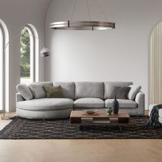 a living room with a large sectional couch and round coffee table in the center, surrounded by arched windows