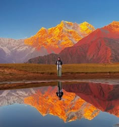 a person standing on the edge of a lake in front of mountains with their reflection