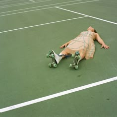 a man laying on top of a tennis court next to two green skateboard wheels