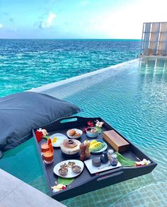 a tray with food on it sitting in the middle of a swimming pool next to an ocean