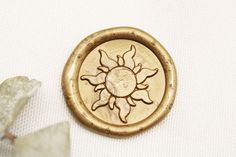 a gold brooch sitting on top of a white cloth covered table next to a piece of paper