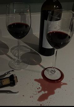 two wine glasses with red wine next to each other on a white counter top,