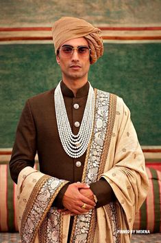 a man wearing a turban and pearls is standing in front of a couch