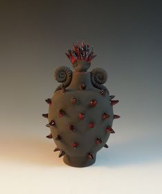 a ceramic vase with spikes on the sides and red stones in the middle, sitting on a white surface